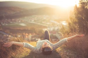 Carefree happy woman lying on green grass meadow on top of mountain edge cliff enjoying sun on her face.Enjoying nature sunset.Freedom.Enjoyment.Relaxing in mountains at sunrise.Sunshine.Daydreaming
